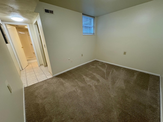 carpeted spare room featuring baseboards, visible vents, a textured ceiling, and tile patterned floors