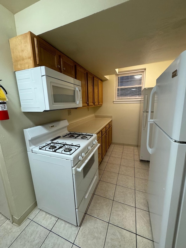 kitchen with light countertops, white appliances, brown cabinetry, and light tile patterned flooring