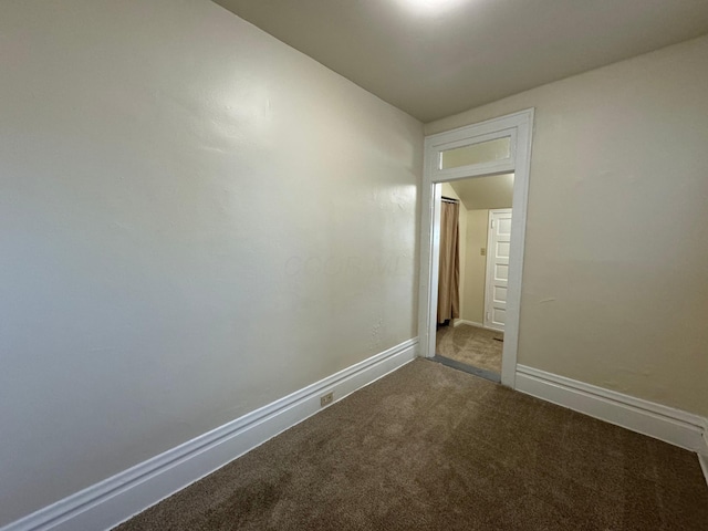 spare room with baseboards and dark colored carpet