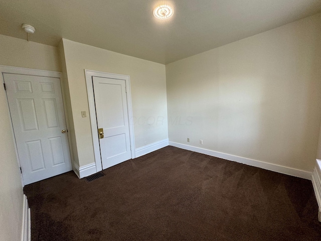 unfurnished bedroom with baseboards, visible vents, and dark carpet