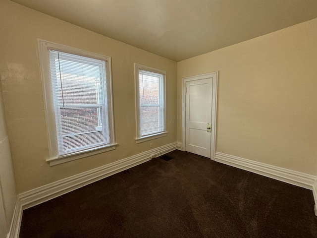 spare room with baseboards and dark colored carpet