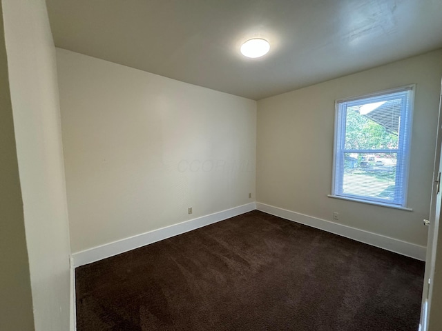 spare room with dark carpet and baseboards