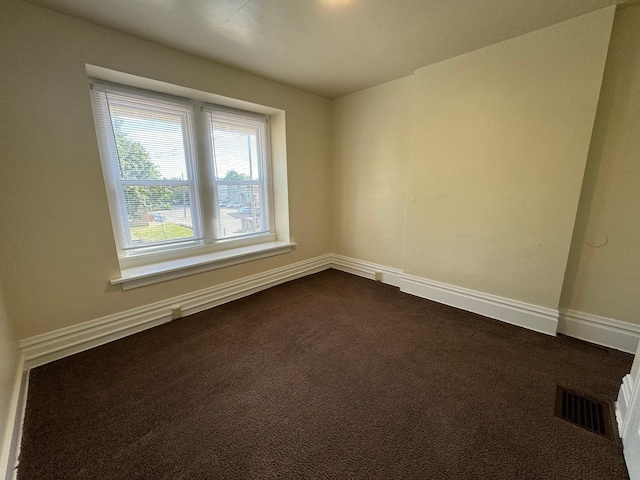 unfurnished room with dark colored carpet, visible vents, and baseboards