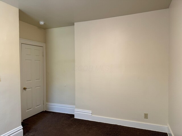 unfurnished room featuring dark carpet and baseboards