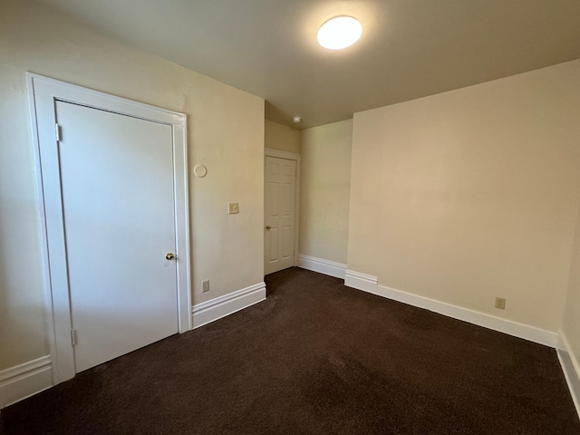 unfurnished bedroom featuring baseboards and dark colored carpet