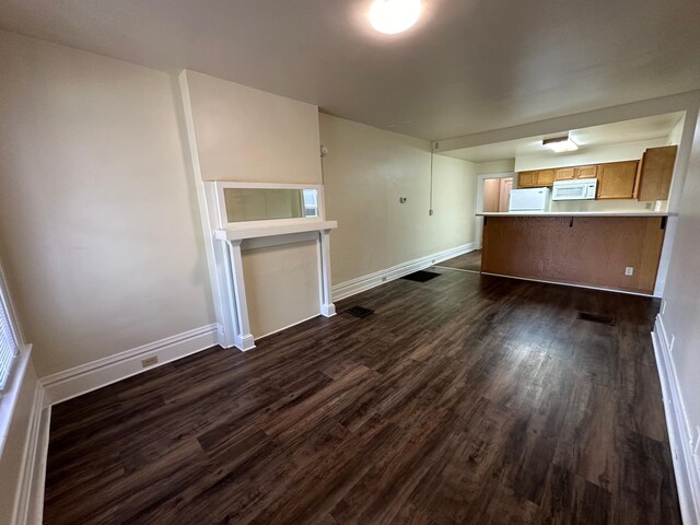 unfurnished living room with dark wood-type flooring and baseboards