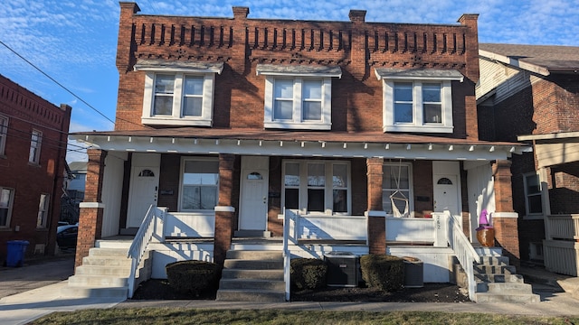 view of front of home with a porch, cooling unit, and brick siding