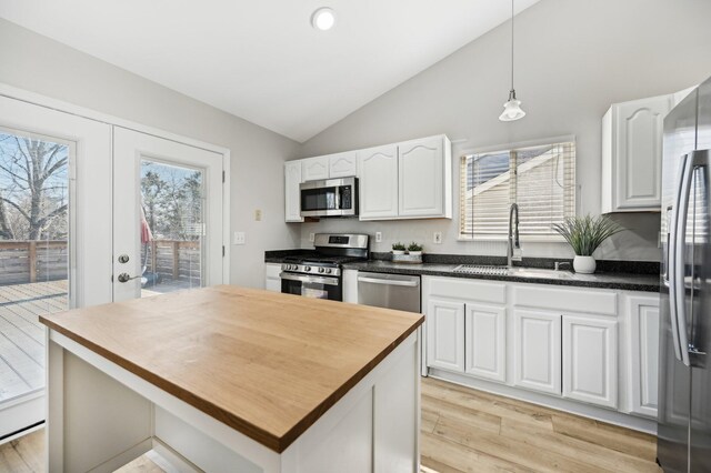 kitchen featuring vaulted ceiling, appliances with stainless steel finishes, white cabinetry, wood counters, and a sink