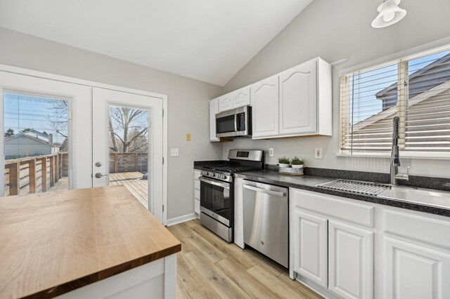 kitchen featuring butcher block countertops, lofted ceiling, stainless steel appliances, white cabinetry, and a sink