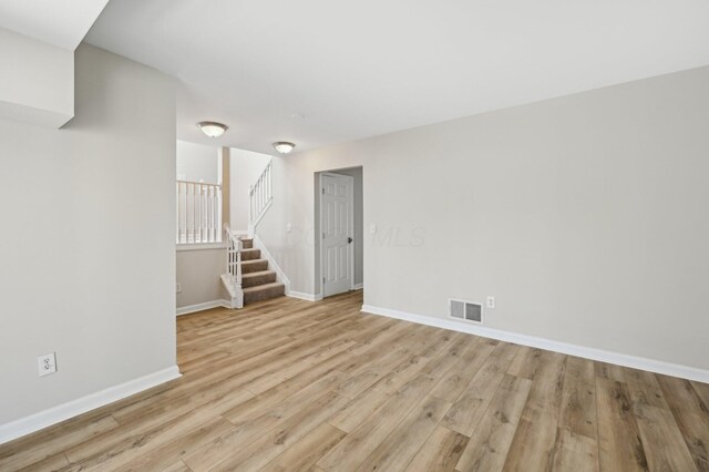 unfurnished room with light wood finished floors, visible vents, stairs, and baseboards