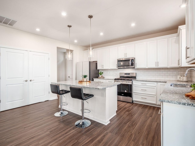 kitchen with stainless steel appliances, a kitchen island, a sink, and white cabinets