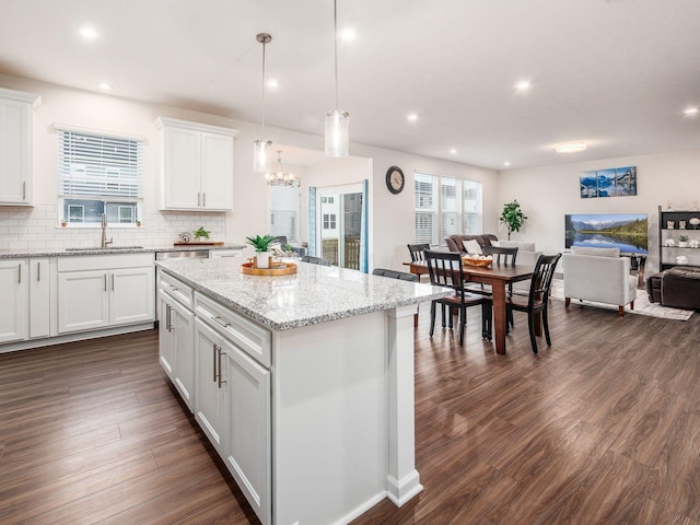 kitchen featuring dark wood-type flooring, a sink, open floor plan, a center island, and tasteful backsplash