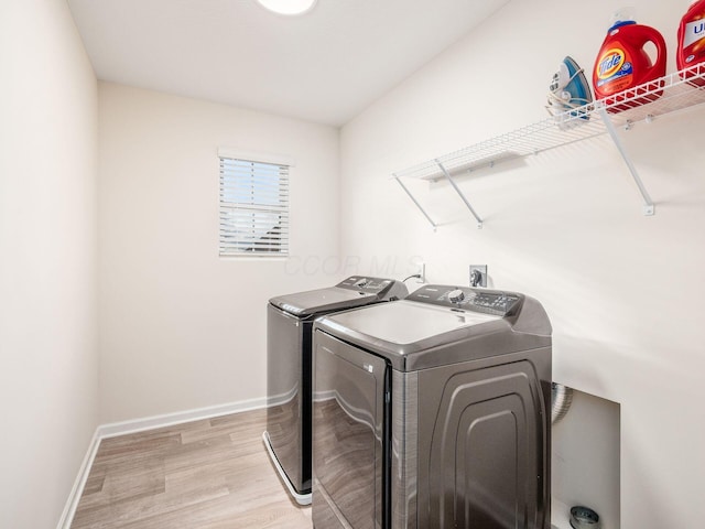 laundry area with laundry area, baseboards, light wood-style flooring, and washing machine and clothes dryer