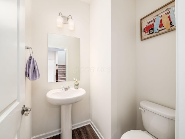 half bath featuring toilet, a sink, baseboards, and wood finished floors