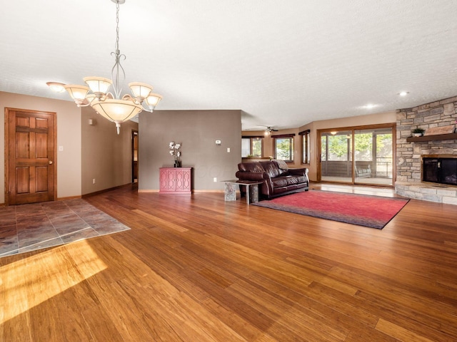 unfurnished living room featuring a chandelier, a stone fireplace, wood finished floors, and baseboards