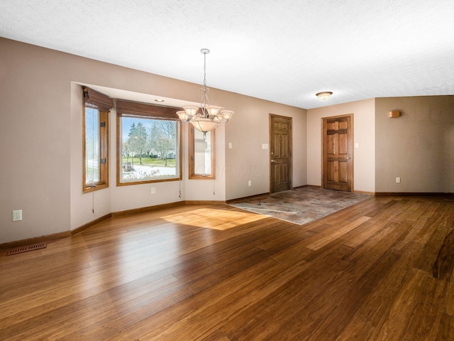 empty room with baseboards, visible vents, a chandelier, and wood finished floors