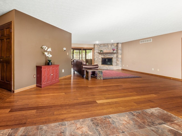 unfurnished living room with visible vents, a fireplace, baseboards, and wood finished floors