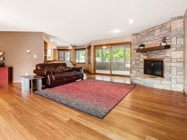 living room with baseboards, a stone fireplace, a textured ceiling, and wood finished floors