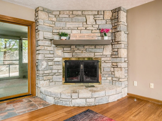 room details with a textured ceiling, a fireplace, wood finished floors, visible vents, and baseboards