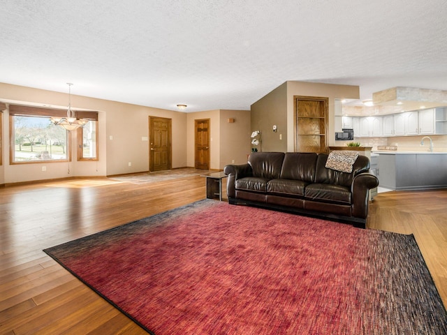 living room with light wood-type flooring, a textured ceiling, baseboards, and an inviting chandelier