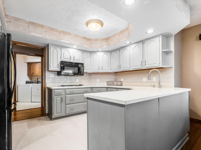 kitchen with open shelves, gray cabinetry, independent washer and dryer, a peninsula, and black appliances