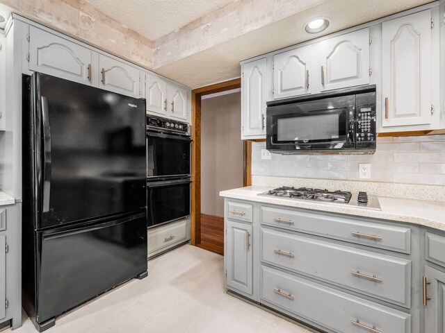 kitchen with gray cabinets, light countertops, a textured ceiling, black appliances, and backsplash