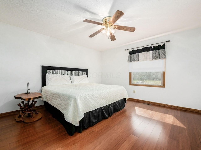 bedroom featuring ceiling fan, wood finished floors, visible vents, and baseboards