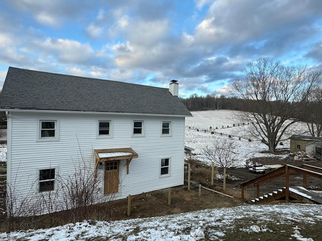 snow covered rear of property with a chimney and roof with shingles