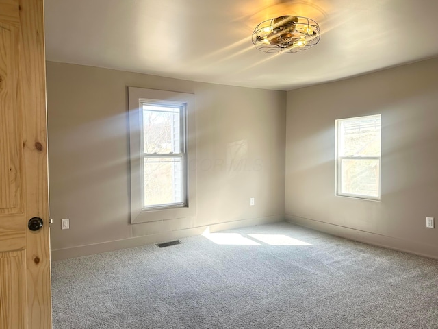 spare room featuring carpet flooring, plenty of natural light, baseboards, and visible vents