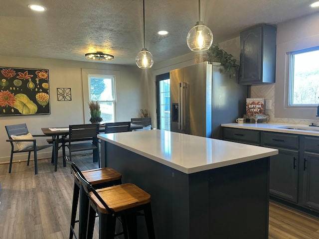 kitchen featuring wood finished floors, high end fridge, a sink, light countertops, and a center island