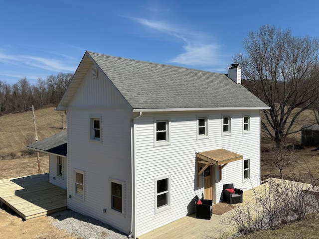 rear view of house featuring a wooden deck, roof with shingles, and a chimney