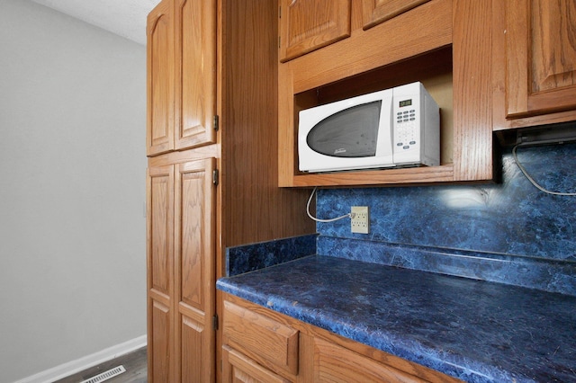 kitchen featuring white microwave, backsplash, dark countertops, and baseboards