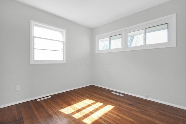 spare room with visible vents, baseboards, and dark wood-style flooring