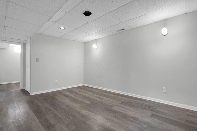 finished below grade area with a paneled ceiling, visible vents, baseboards, and dark wood-style flooring