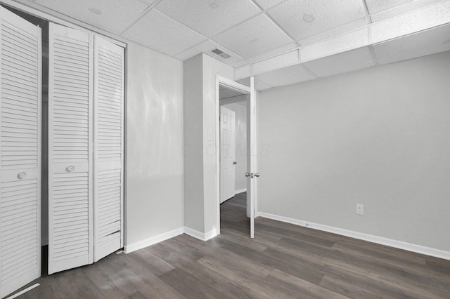 unfurnished bedroom featuring visible vents, a drop ceiling, dark wood finished floors, a closet, and baseboards