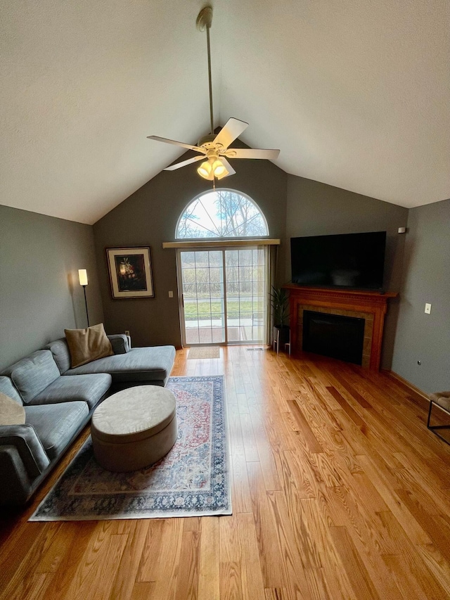 living area with ceiling fan, a fireplace, vaulted ceiling, and wood finished floors