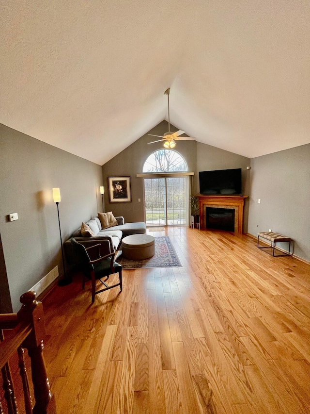 living area featuring a fireplace, lofted ceiling, light wood-style floors, ceiling fan, and baseboards