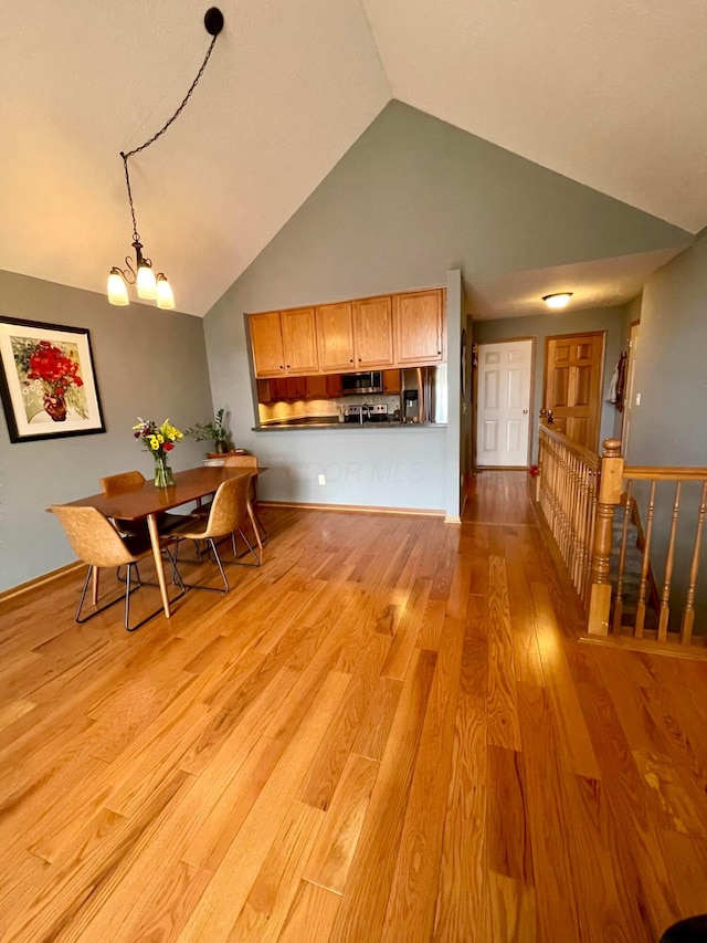 interior space featuring decorative light fixtures, high vaulted ceiling, stainless steel microwave, light wood-style flooring, and a chandelier