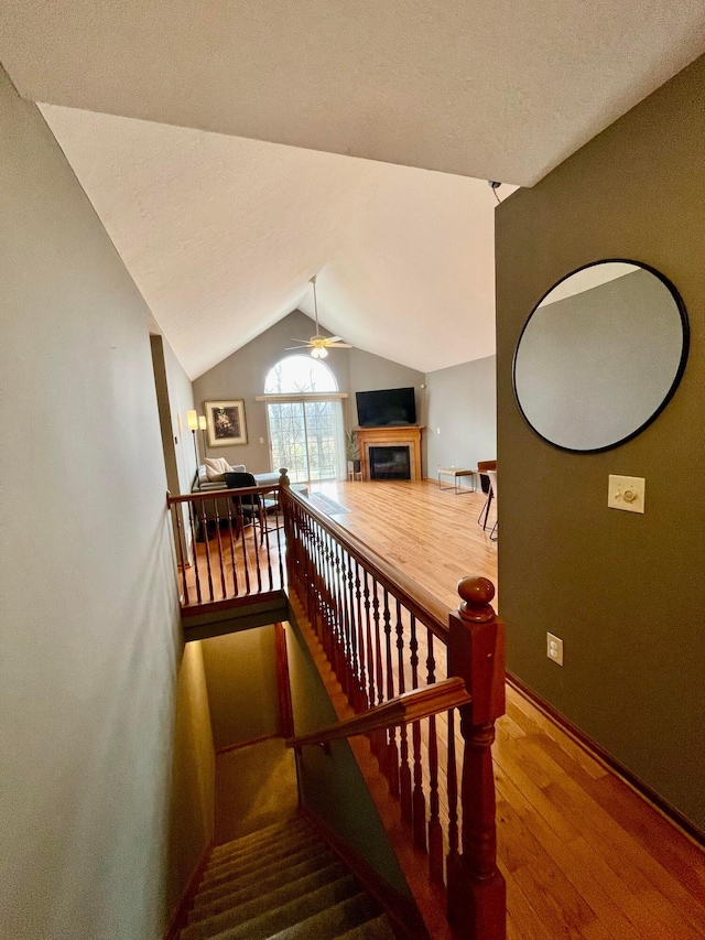 stairway with vaulted ceiling, a fireplace, wood finished floors, and a ceiling fan