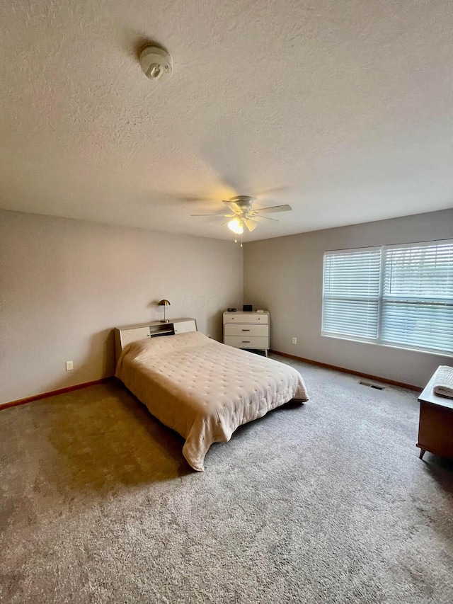 carpeted bedroom featuring baseboards, a textured ceiling, visible vents, and a ceiling fan