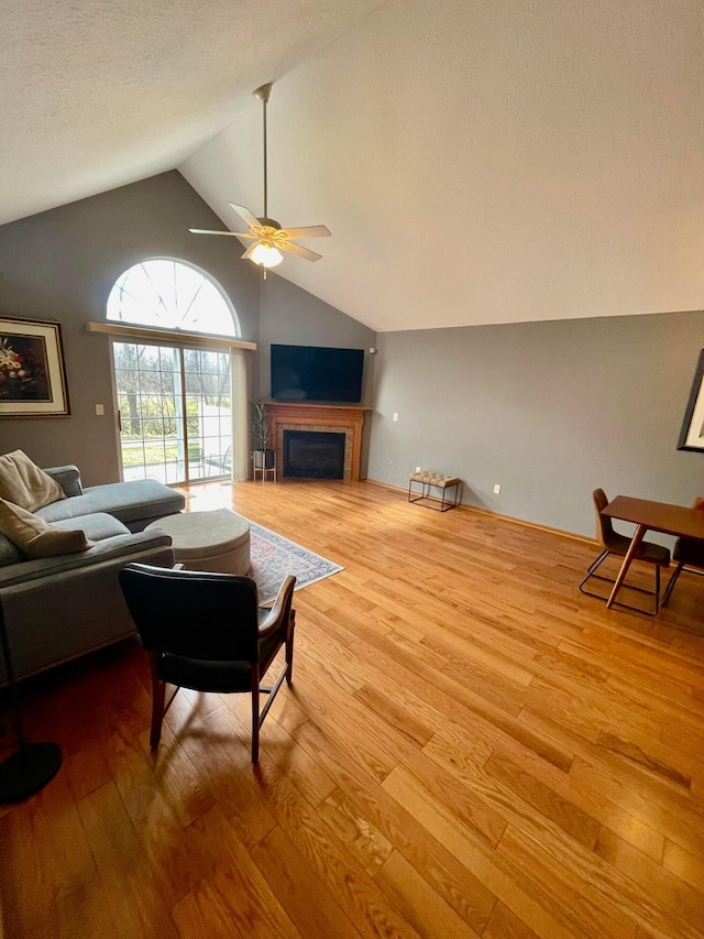 living room featuring ceiling fan, high vaulted ceiling, a fireplace, and wood finished floors