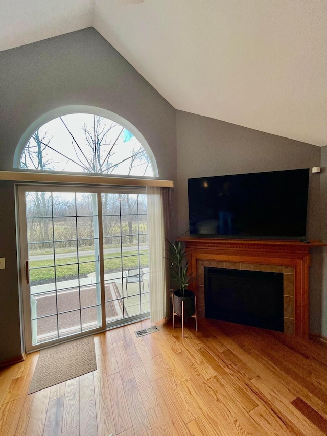 unfurnished living room with lofted ceiling, light wood finished floors, visible vents, and a tile fireplace