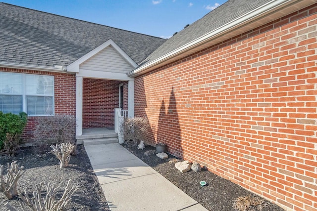 doorway to property featuring brick siding and a shingled roof