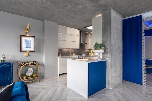 kitchen featuring tasteful backsplash, modern cabinets, light countertops, wall chimney range hood, and white cabinetry