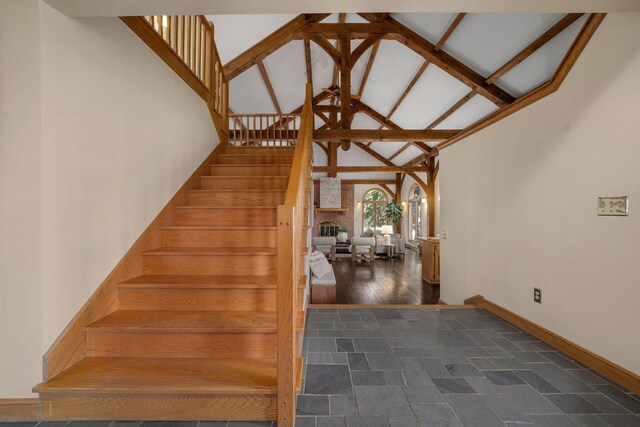 stairs featuring a large fireplace, baseboards, high vaulted ceiling, and beam ceiling