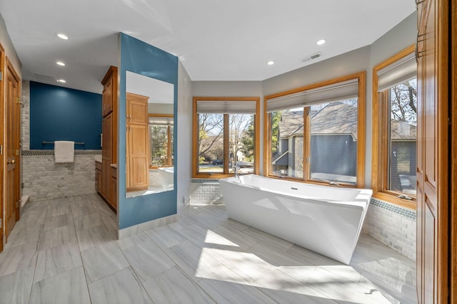 bathroom featuring a wealth of natural light, a soaking tub, and visible vents