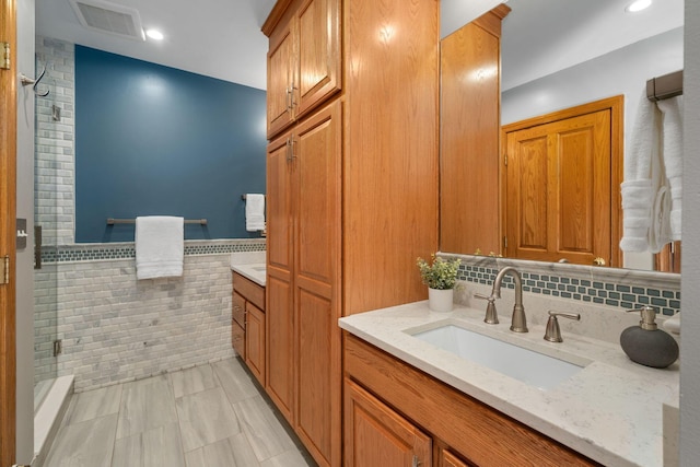 full bathroom with visible vents, vanity, tile walls, wainscoting, and a shower stall