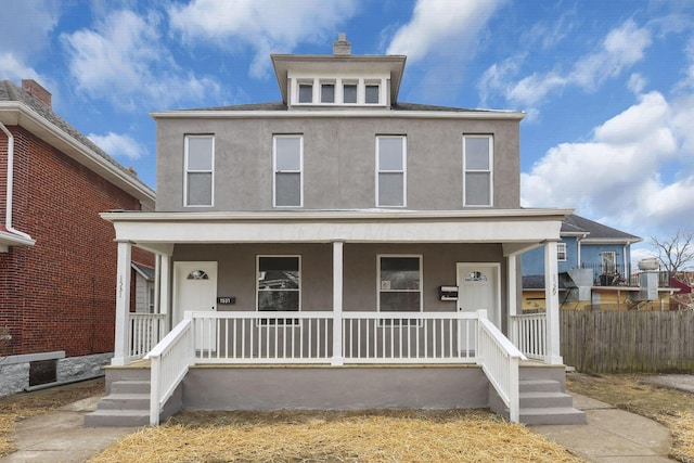 american foursquare style home with covered porch, fence, and stucco siding