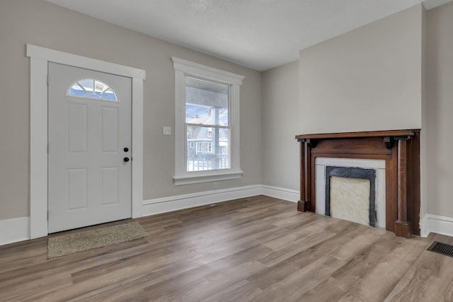 foyer entrance with visible vents, a fireplace, baseboards, and wood finished floors