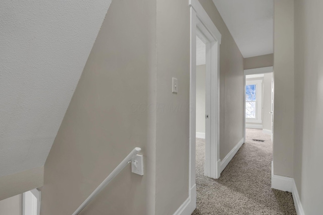 hall featuring carpet, an upstairs landing, visible vents, and baseboards